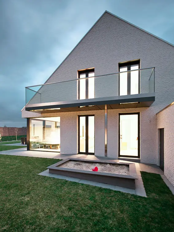 Au&szlig;enperspektive der Giebelseite mit verglastem Balkon. Sandkasten und Rasen im Vordergrund