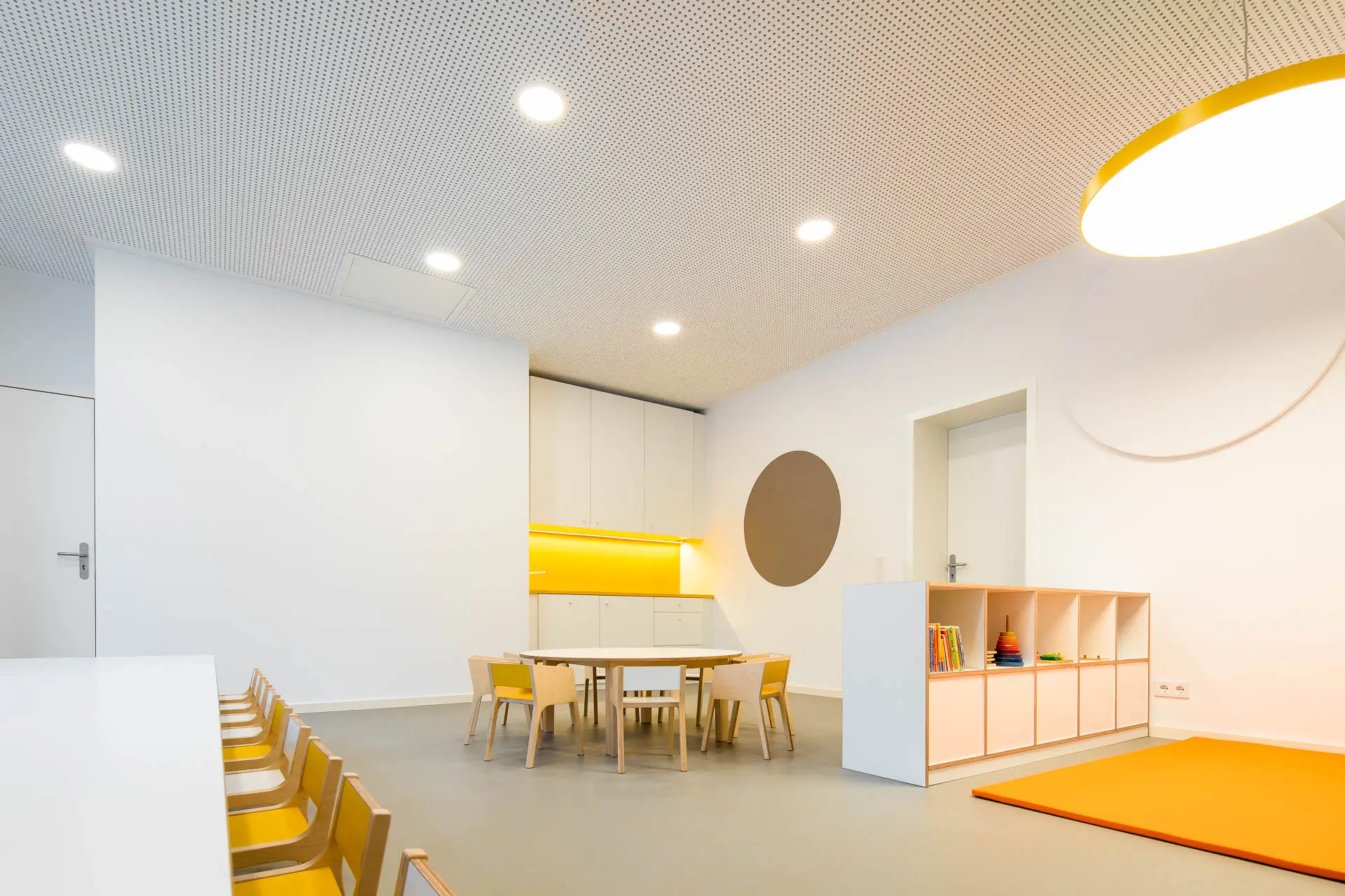 Innenraumperspektive eines Gruppenraums mit gelben Akzenten